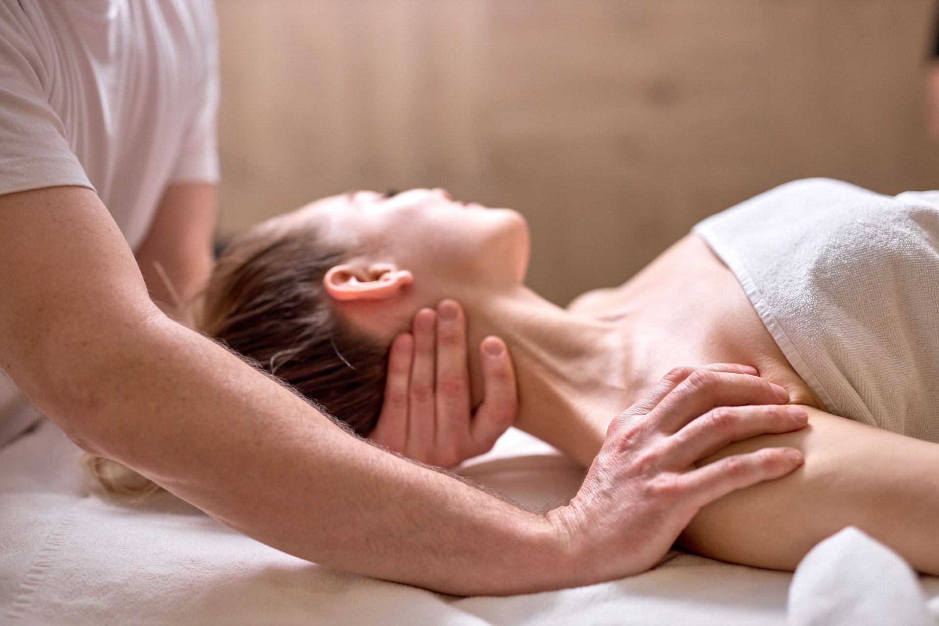 Professional cropped therapist doing healthy massage on neck and shoulders to female client